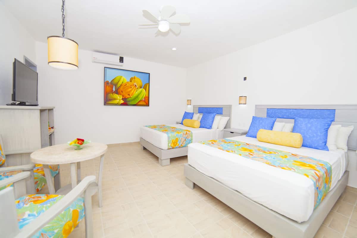 A hotel room with two beds, a TV, a ceiling fan, and a painting on the wall.