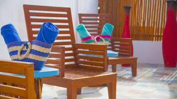 A row of wooden chairs with folded towels and a woven bag on them, arranged on a tiled floor.