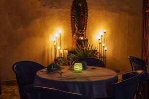 A round dining table with a white tablecloth, surrounded by four chairs. There are candles and a decorative glass on the table.