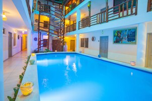 A multi-level indoor swimming pool with a wooden staircase, multiple balconies, and a large mural on the wall.