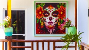 Ein gerahmtes Bildnis eines Día-de-Muertos-Gesichts mit Blumen auf einem Balkongeländer.