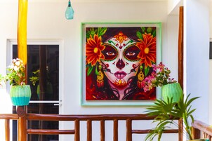 A framed painting of a Day of the Dead style face with flowers on a balcony railing.