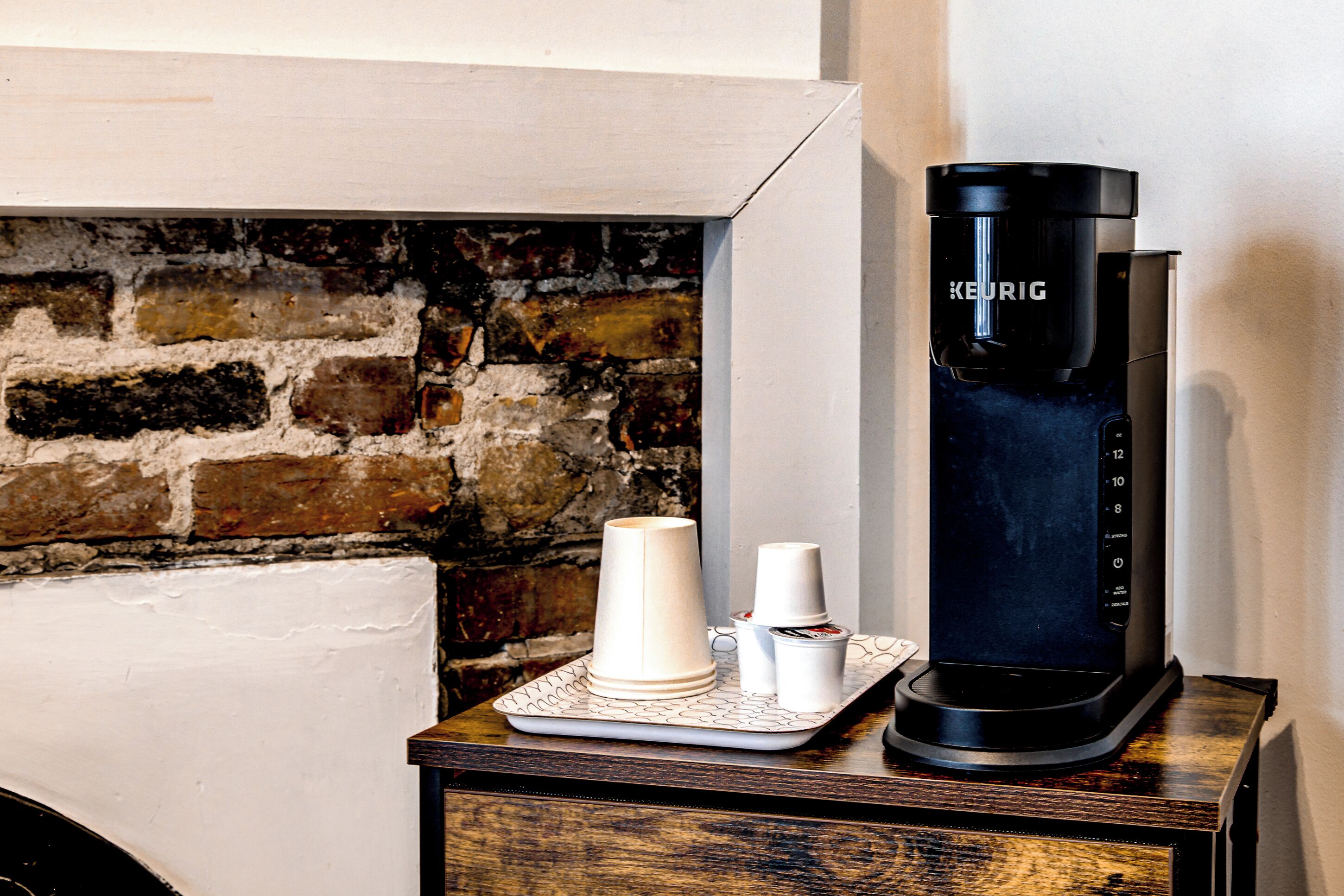 Uma máquina de café sobre uma mesa de madeira com um tabuleiro, ao lado de uma parede de tijolos.