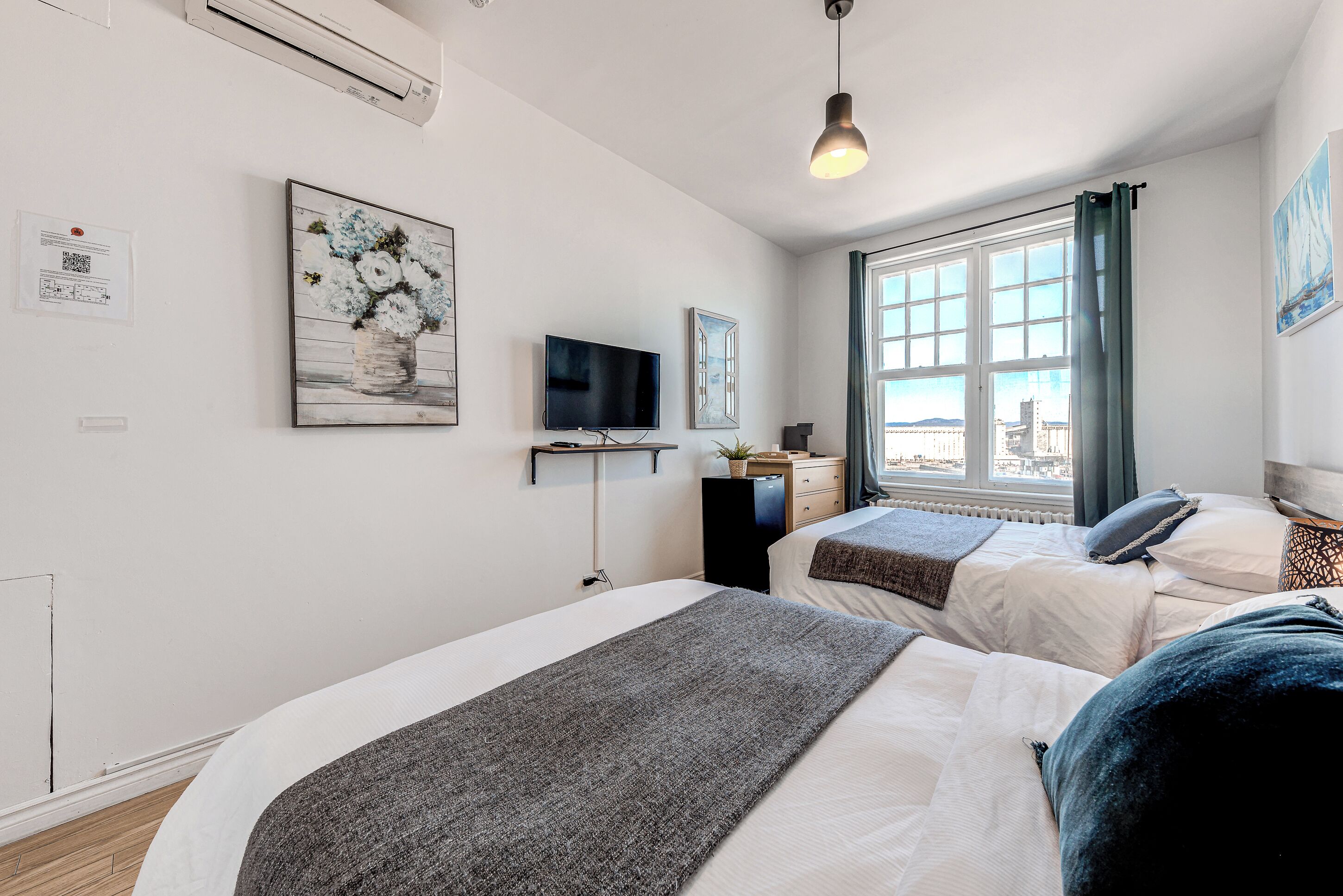 Ein modernes Hotelzimmer mit zwei Betten, einem Fernseher und einem großen Fenster mit Blick auf die Stadt.