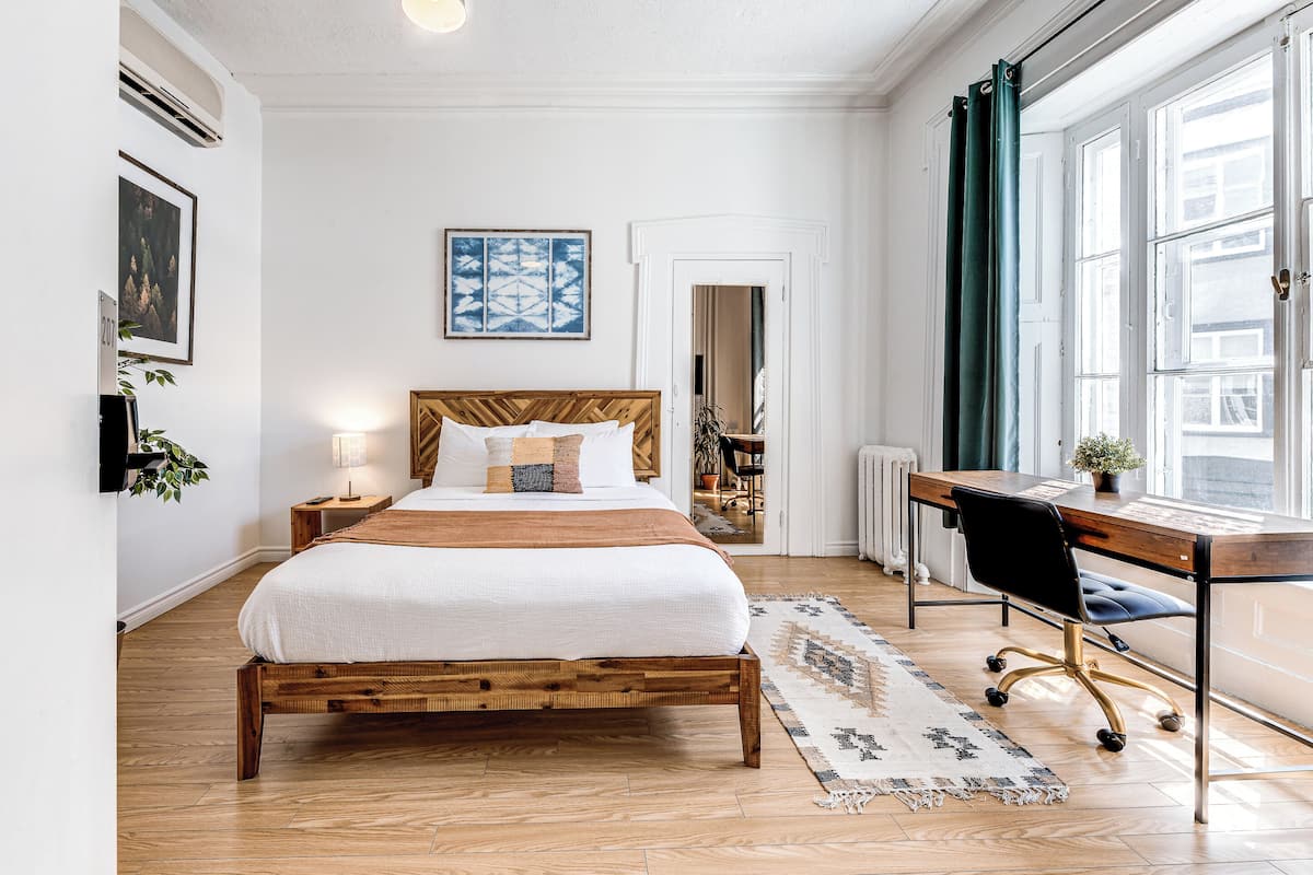 A bedroom with a wooden bed, a desk, and a large window.