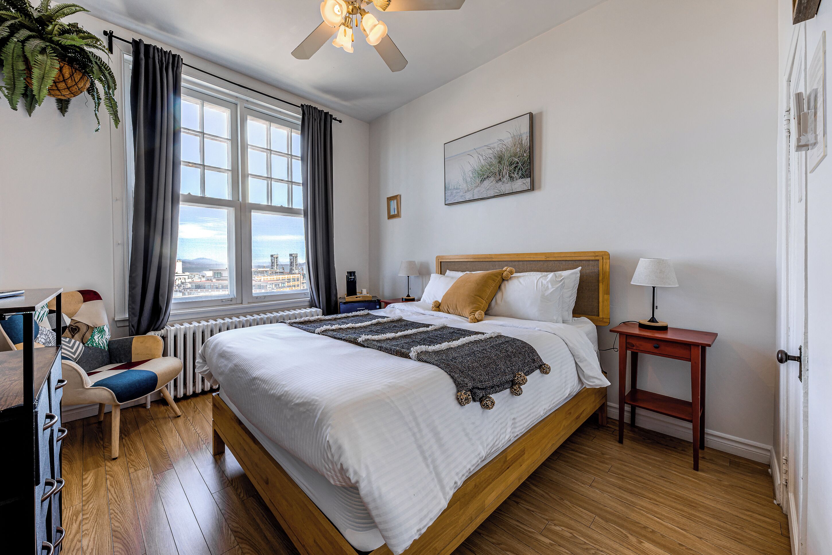 A neatly arranged bedroom with a large bed, a bedside table, a chair, and a window with curtains.