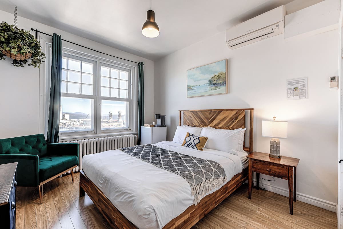 A bedroom with a large bed, a green sofa, a wooden nightstand, and a window with a city view.