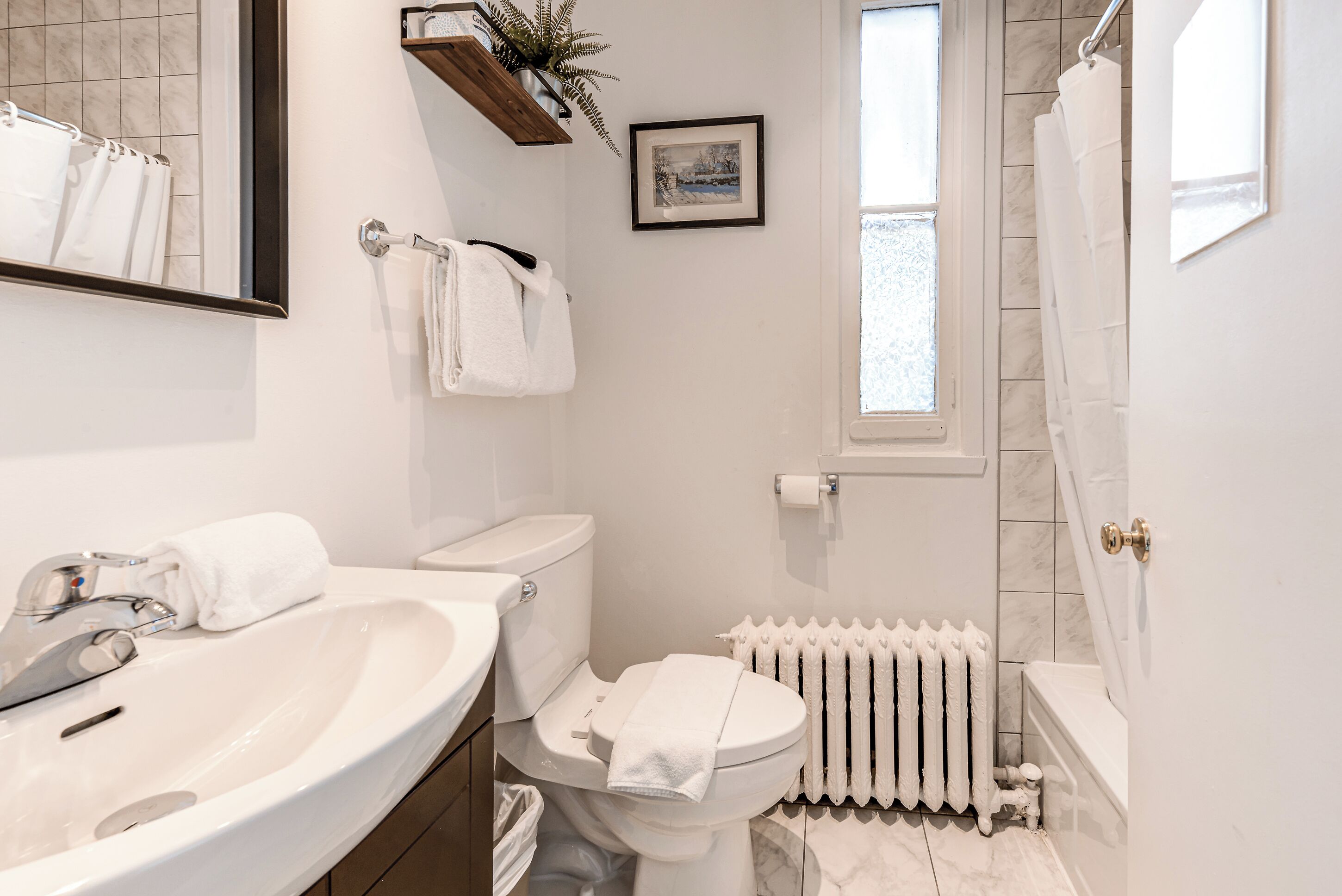 A bathroom with a white sink, toilet, and bathtub, a radiator, and a framed picture on the wall.