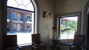 A room with two armchairs, a small table with a vase, and a large arched window offering a view of a building and greenery outside. - Hotel Fiesta Navojoa (Navojoa)