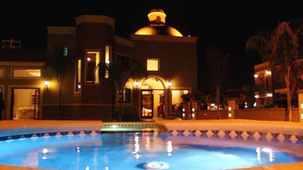 A swimming pool with a tiled edge, surrounded by buildings with illuminated windows and a central dome structure. - Hotel Fiesta Navojoa (Navojoa)
