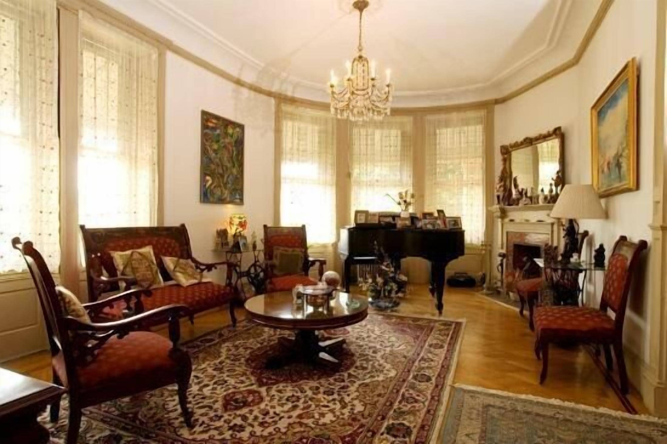 A spacious living room with a grand piano, elegant furniture, and a chandelier.