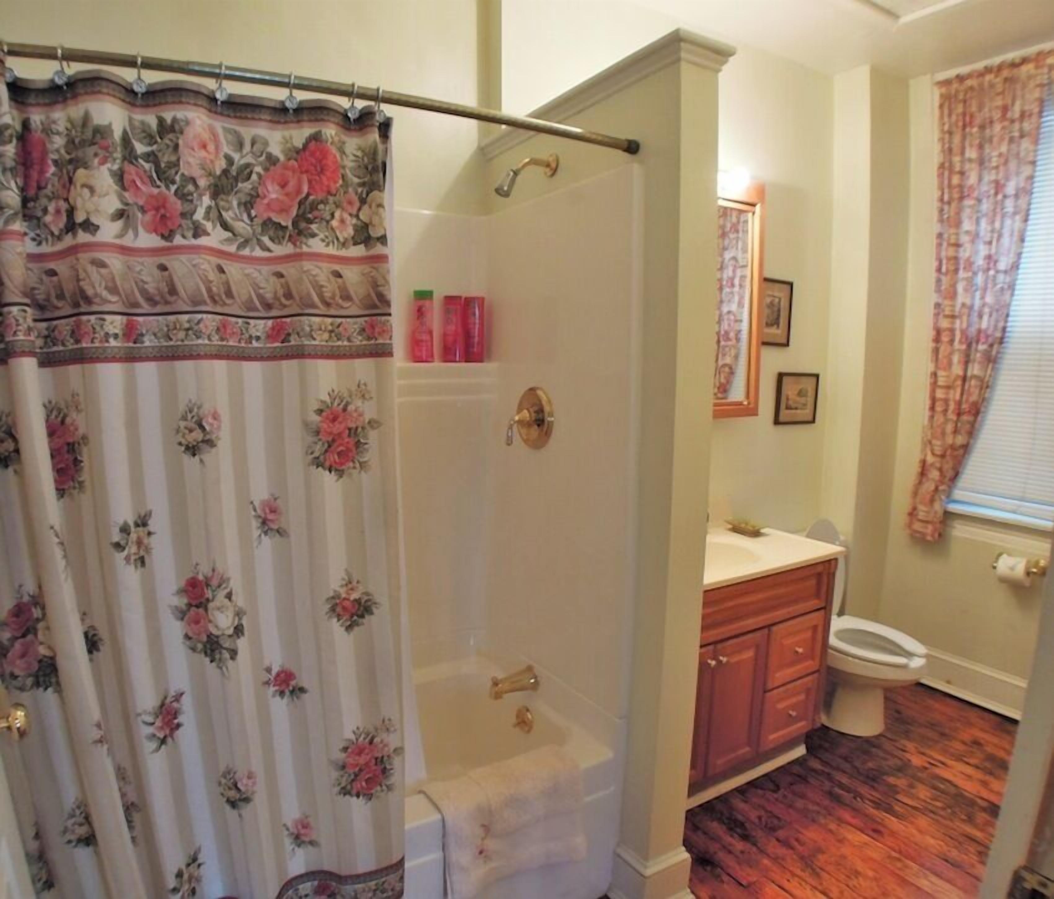 A bathroom with a shower curtain, a bathtub, a toilet, and wooden cabinets.