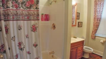 A bathroom with a shower curtain, a bathtub, a toilet, and wooden cabinets.