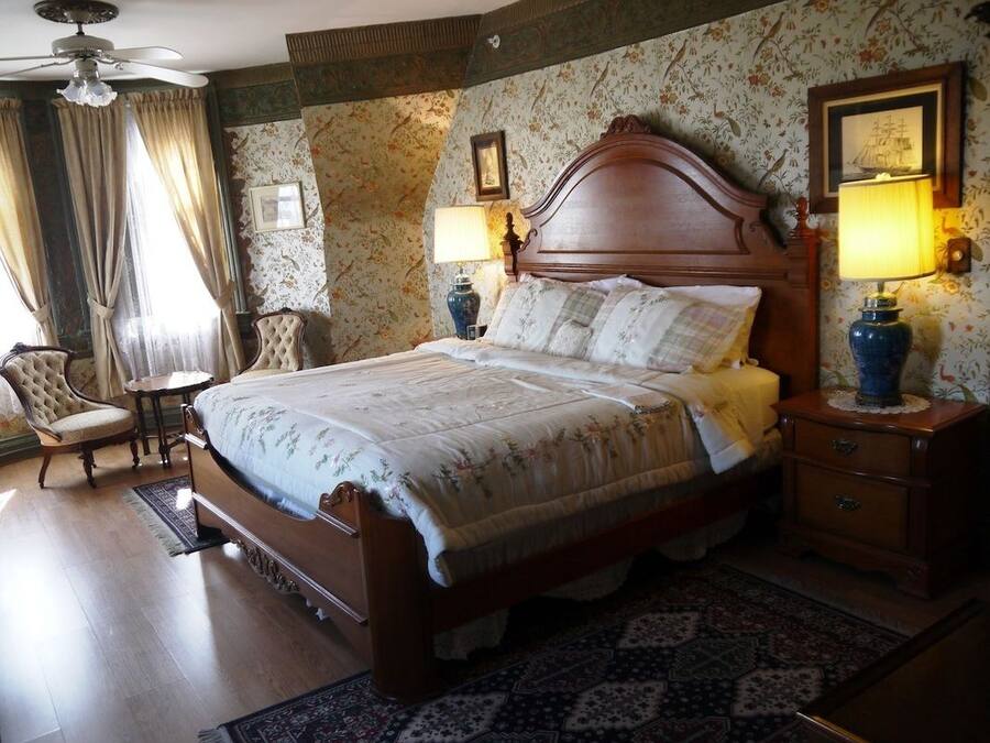 A classic bedroom with a wooden bed, two bedside tables with lamps, a chair, and a patterned rug.