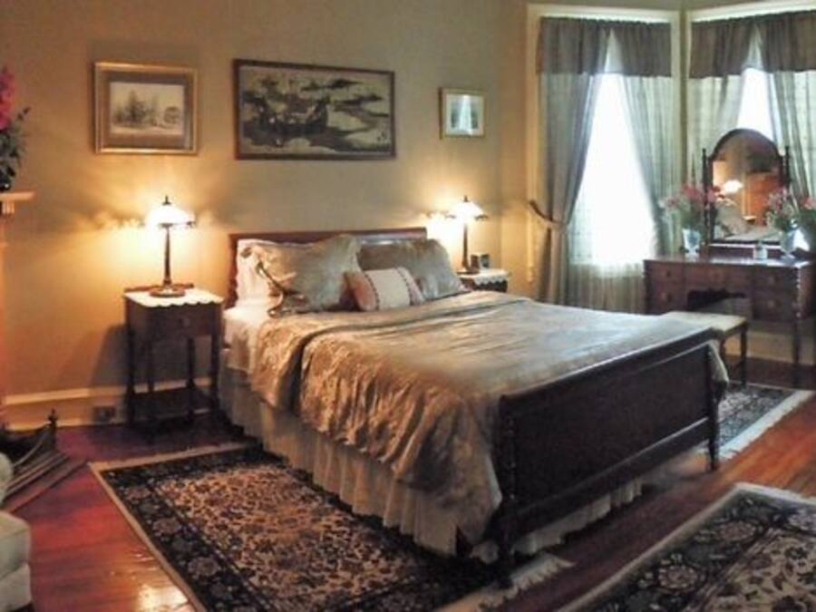 Un dormitorio con una cama grande, una silla, una mesita de noche, un aparador y un espejo.