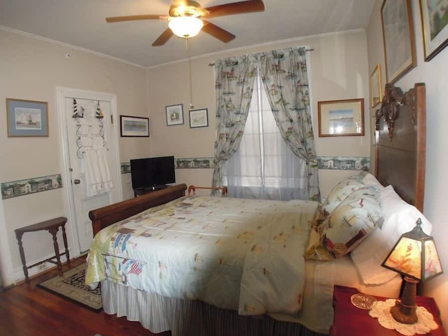 Un dormitorio con cama, televisor, ventilador de techo y ventana con cortinas.