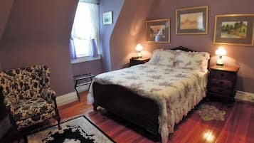 Un dormitorio con cama, mesitas de noche, una silla y una ventana con cortinas.