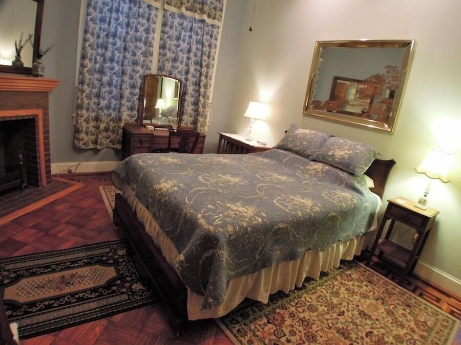 A bedroom with a large bed, a fireplace, a mirror, and a painting on the wall.
