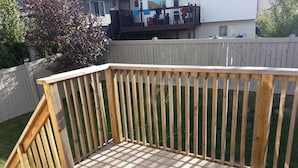 A wooden deck with a railing, surrounded by a white fence and a lawn. - Pinnacle Guest House (Grande Prairie)