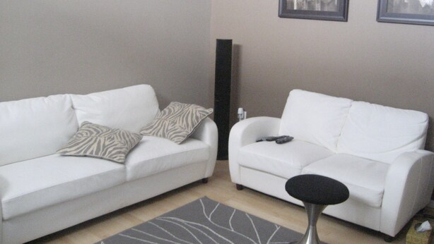 Two white sofas with patterned cushions, a black floor lamp, and a gray rug with white lines. - Pinnacle Guest House (Grande Prairie)