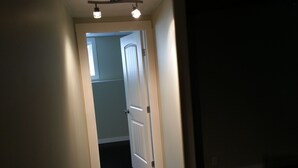 A narrow hallway with a door at the end, a ceiling light fixture, and a visible door handle. - Pinnacle Guest House (Grande Prairie)