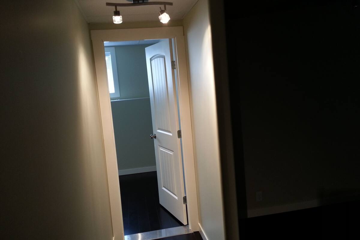 A narrow hallway with a door at the end, a ceiling light fixture, and a visible door handle.