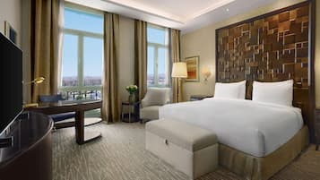 A hotel room with a large bed, a desk, a chair, a TV, and a view of the city.
