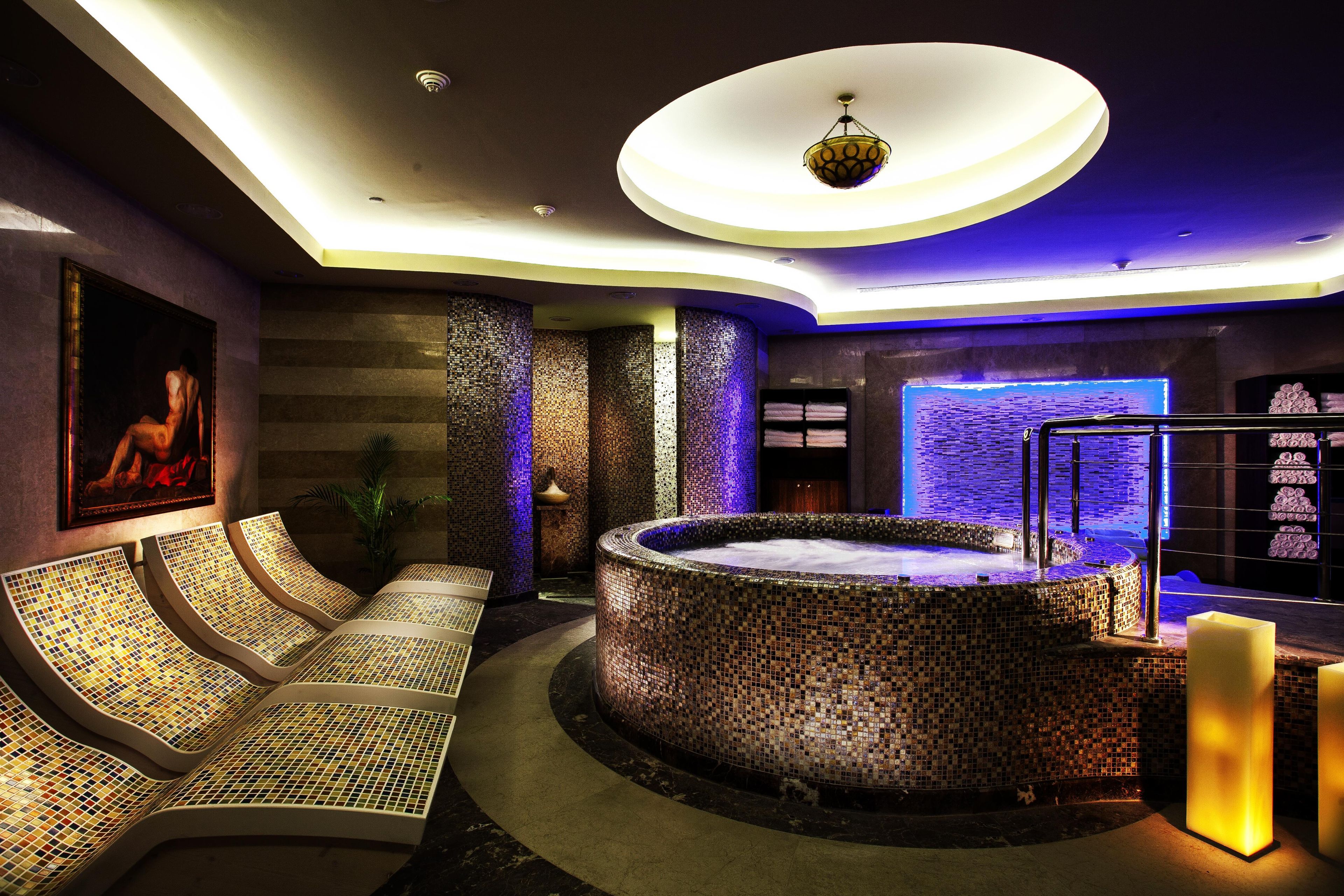 Un área de spa con un jacuzzi con mosaicos, un rincón de estar con cojines estampados y un cuadro colgado en la pared.