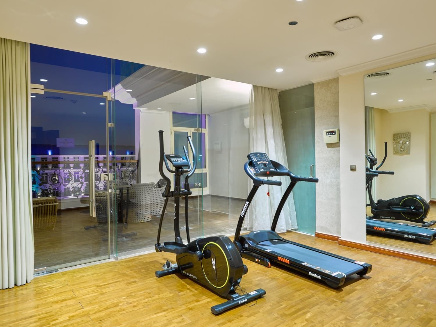 A modern gym with cardio equipment, a glass wall, and a view of the cityscape.