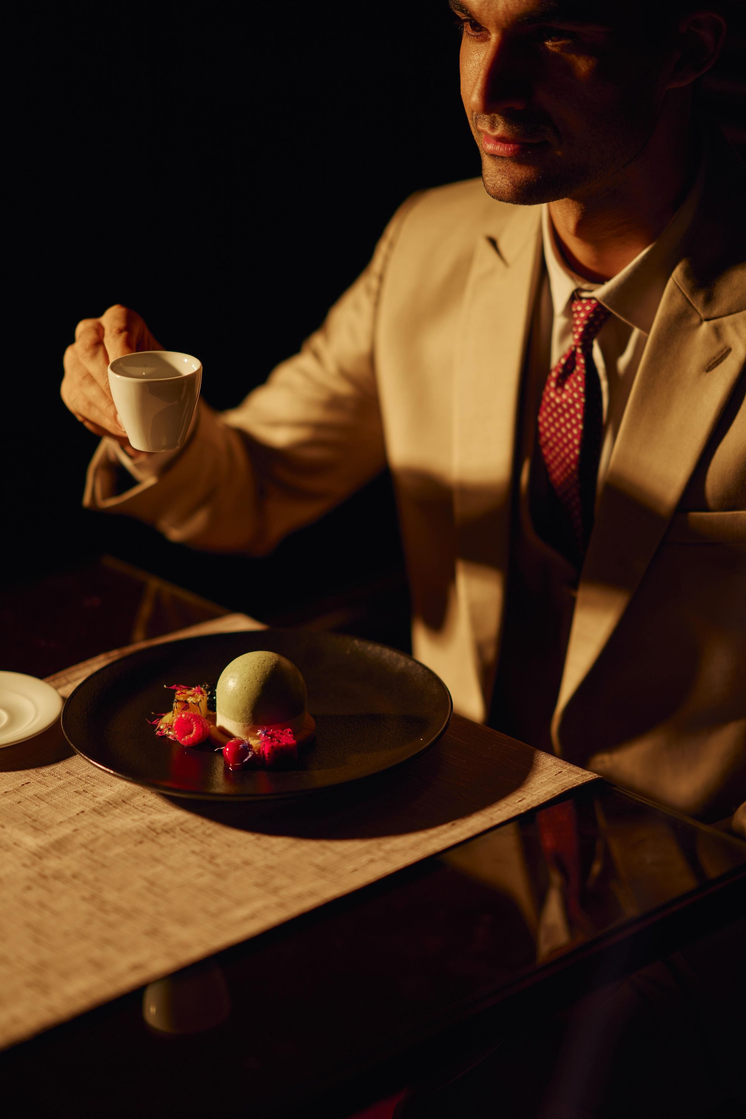 A person seated at a table with a cup and a plate of food.