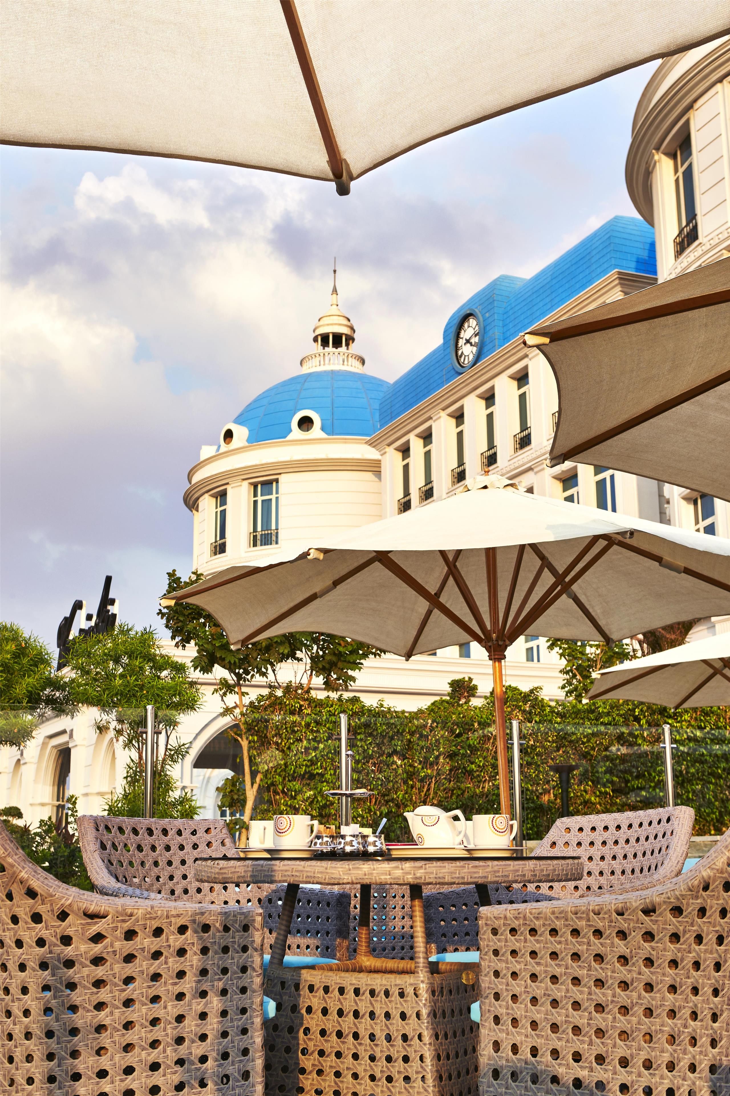 A covered outdoor seating area with wicker furniture, a clock tower in the background, and a clear sky.