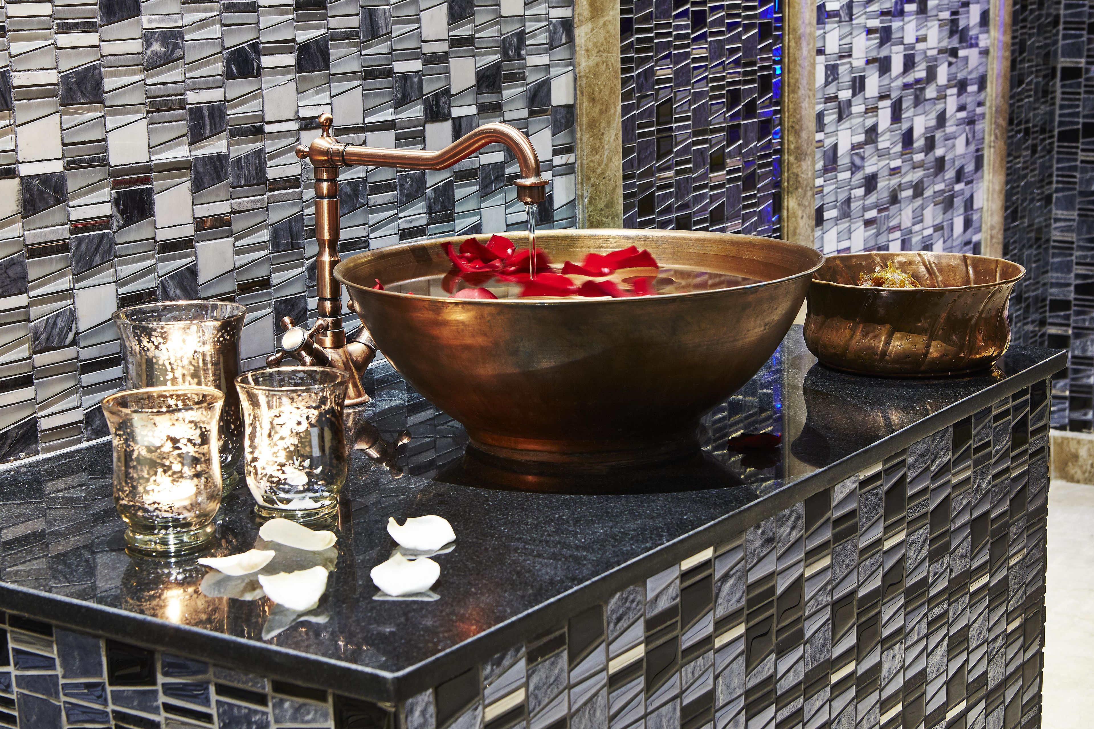 A bathroom with a copper basin, a glass pitcher, and a small bowl on a black countertop.