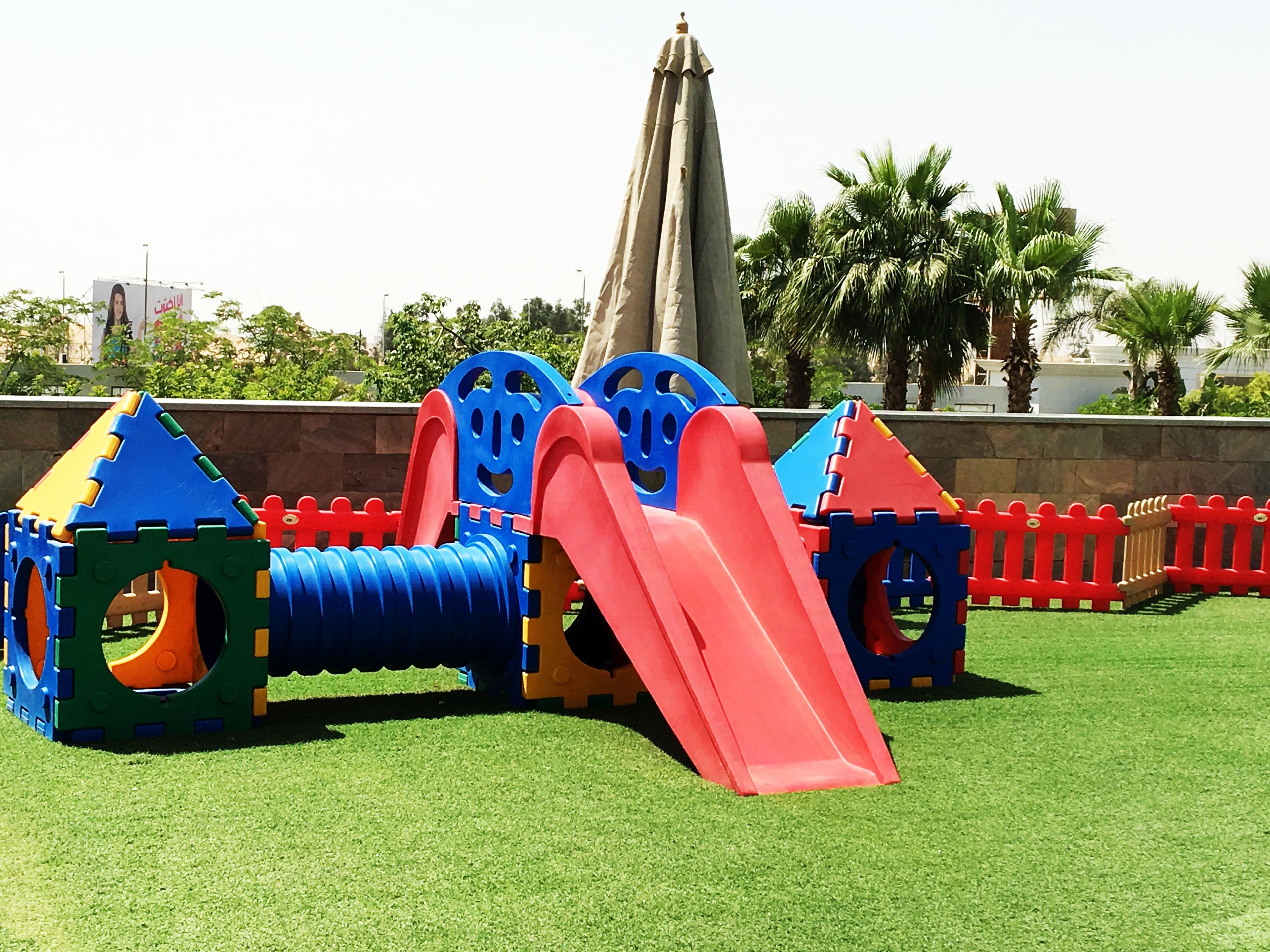 A playground with slides and climbing structures on artificial grass.