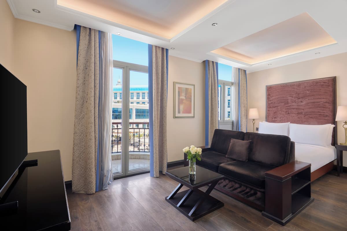 A modern hotel room with a large bed, a sofa, a coffee table, and a TV.