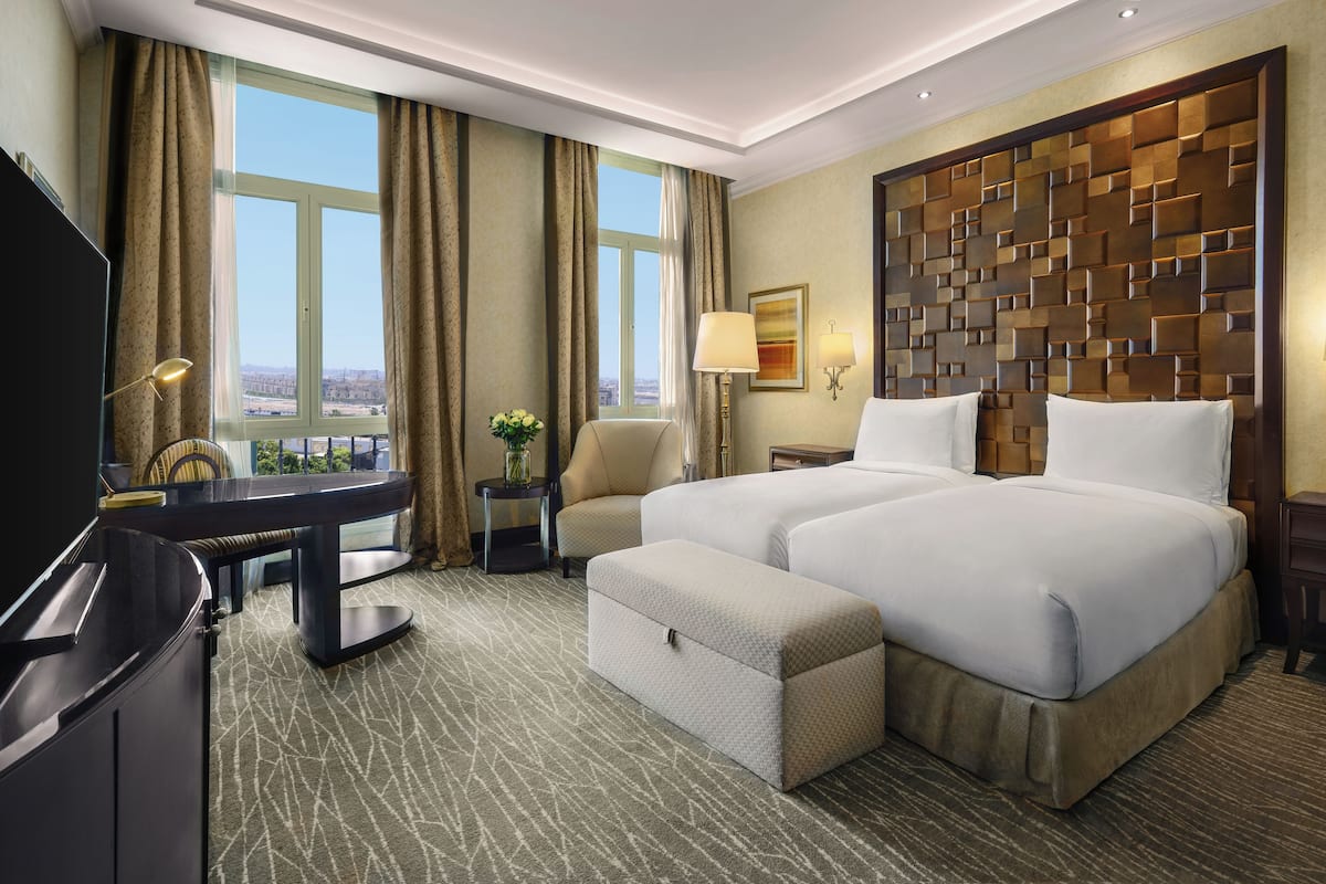 A hotel room with a large bed, a desk, a chair, a TV, and a view of the city.