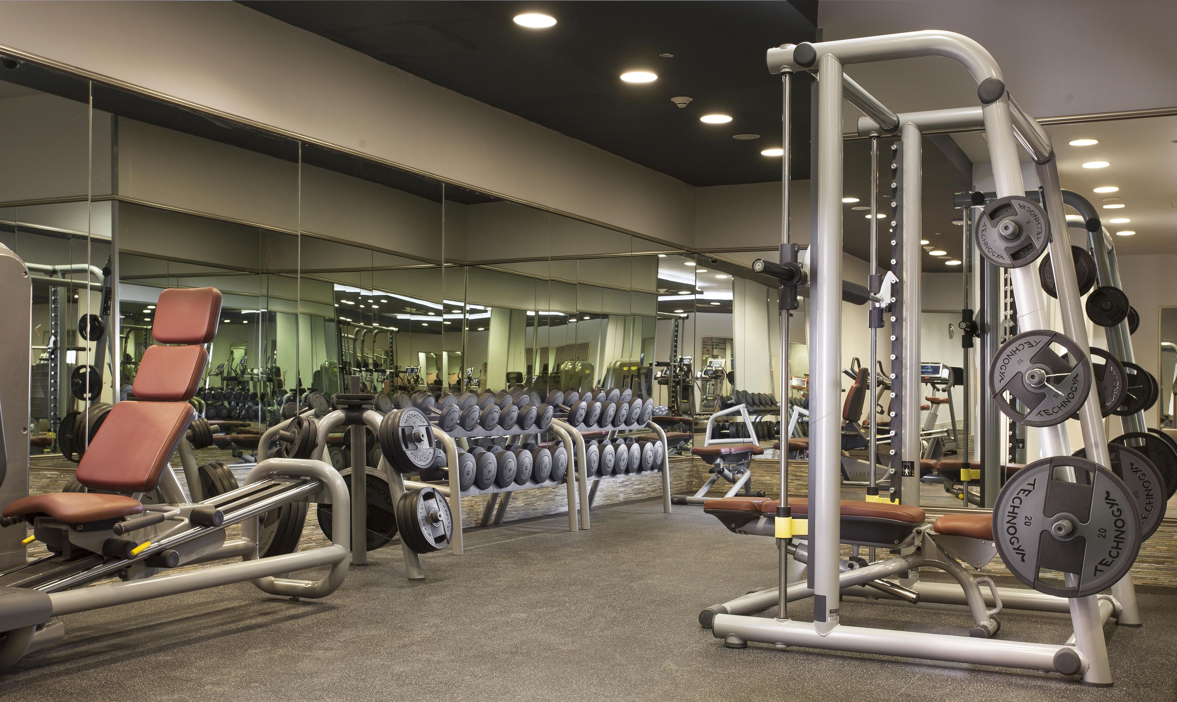 A gym with various exercise equipment, mirrors, and a weightlifting area.