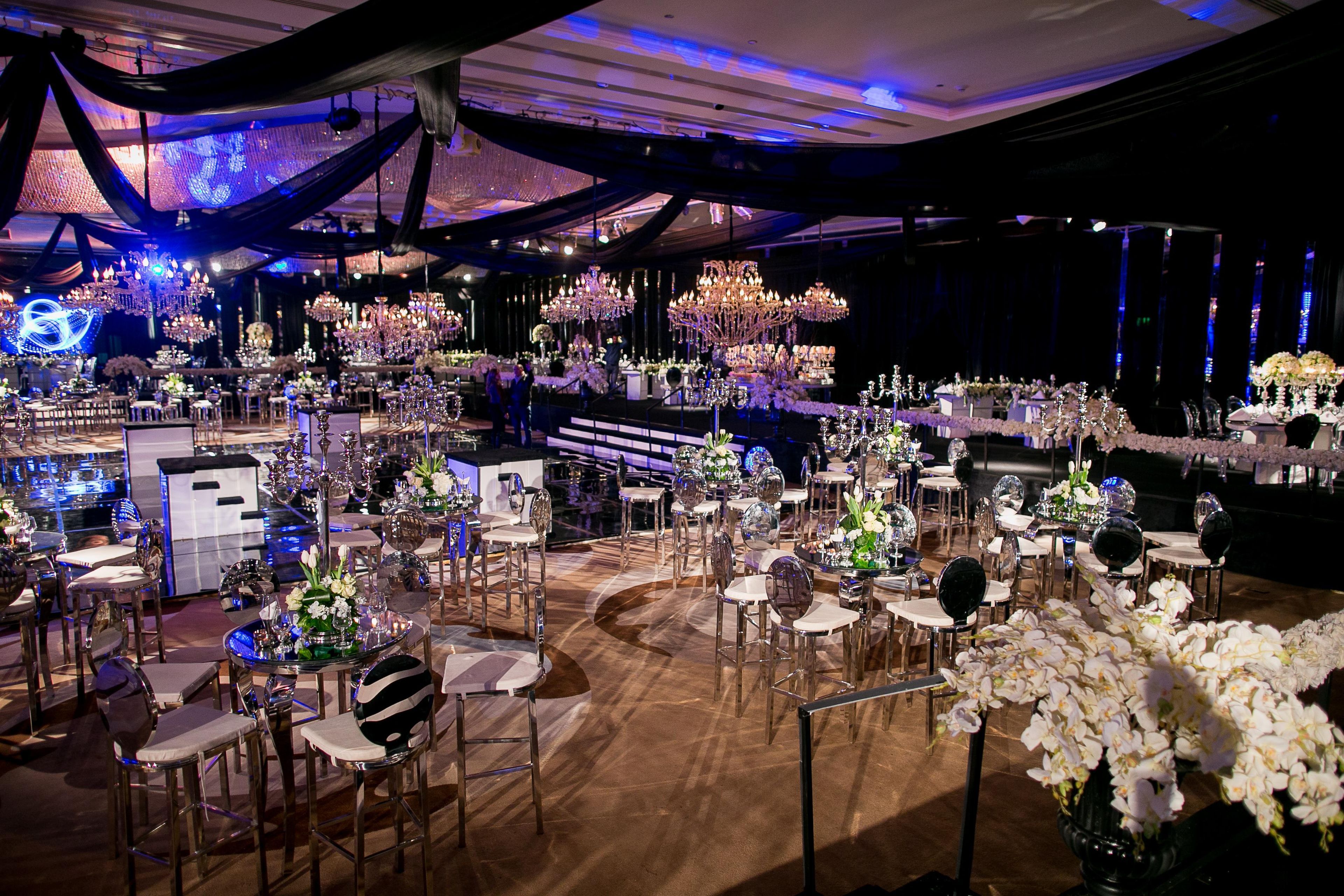 A banquet hall with round tables, chairs, and chandeliers.