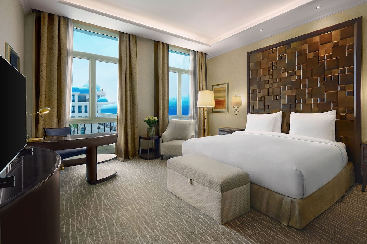 A hotel room with a large bed, a desk, a chair, a TV, and a view of a building with a dome.