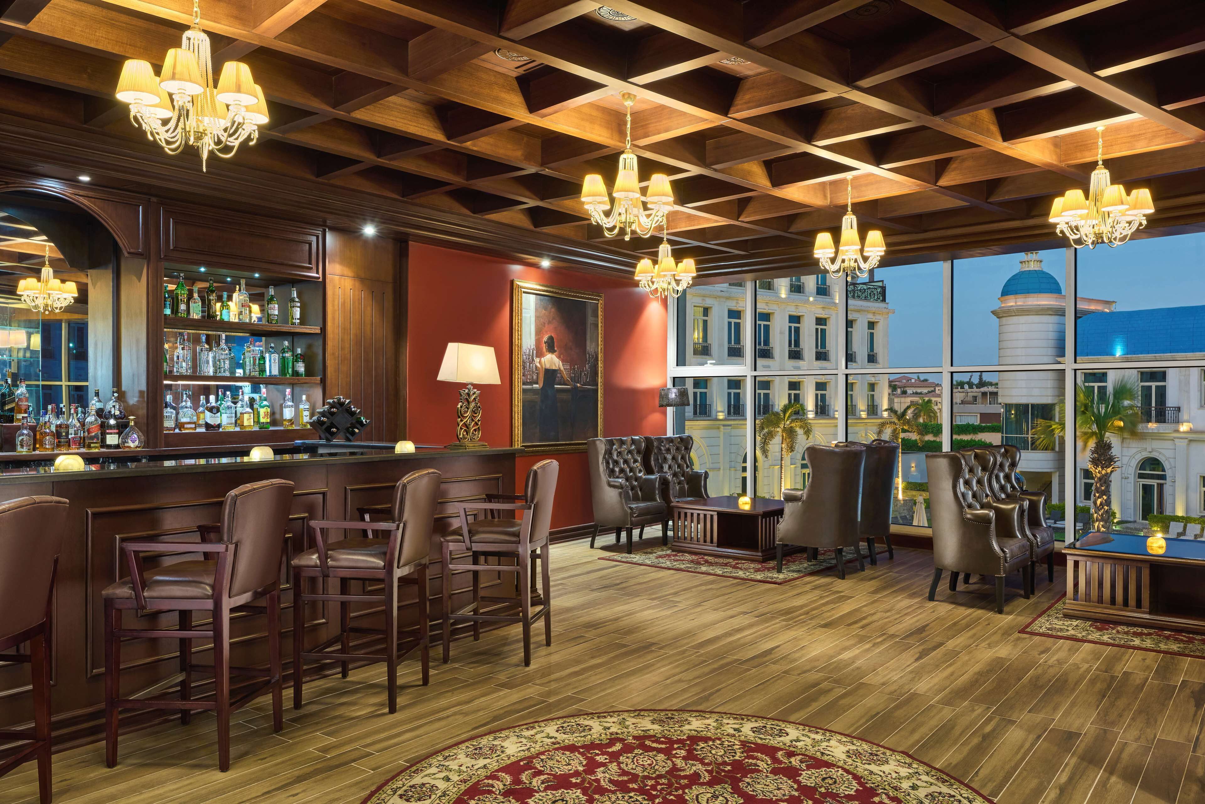 Een bar met houten plafond, barstoelen en een groot raam met uitzicht op gebouwen.