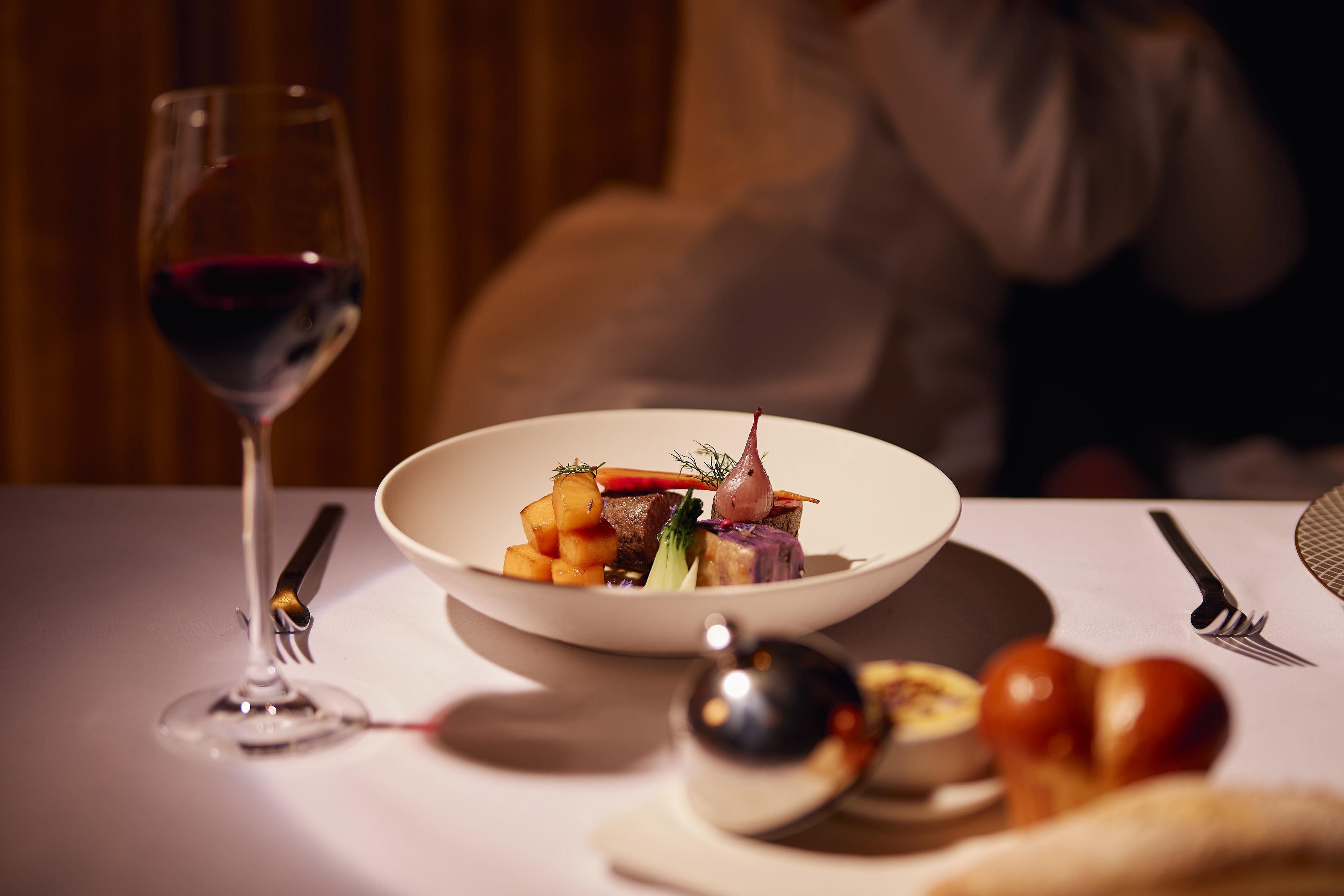 A dining table with a white plate of food, a wine glass, and cutlery.