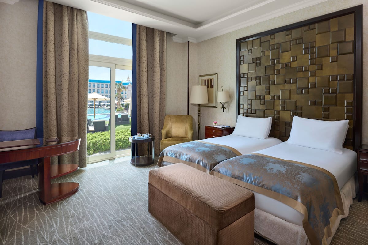 A hotel room with a large bed, a sofa, a desk, and a view of a pool and buildings.