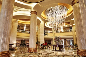 A grand lobby with marble columns, a large chandelier, and a checkered floor pattern. - Kempinski Palace Cairo (New Cairo)