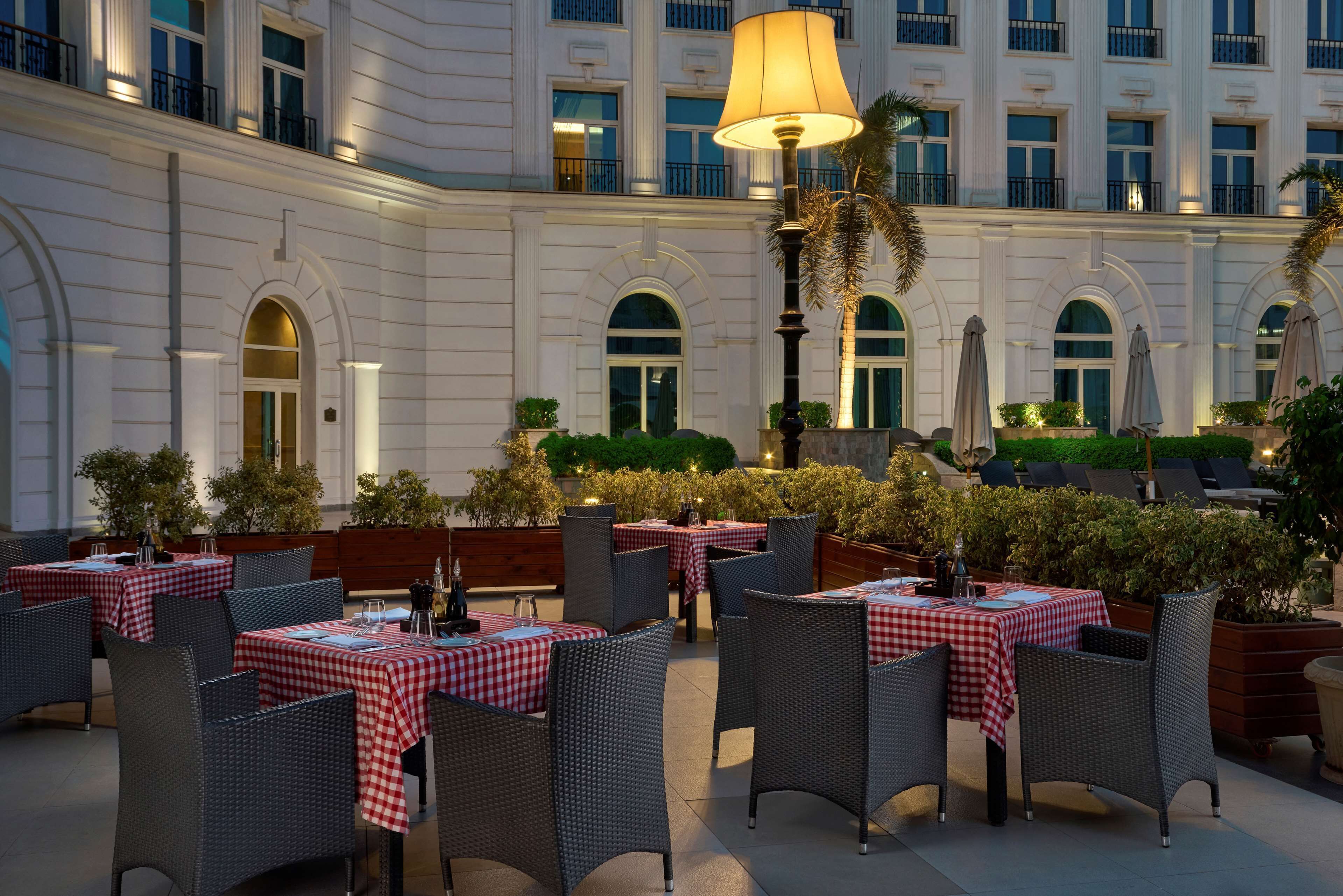 An outdoor dining area with checkered tablecloths, wicker chairs, and a large lamp post.