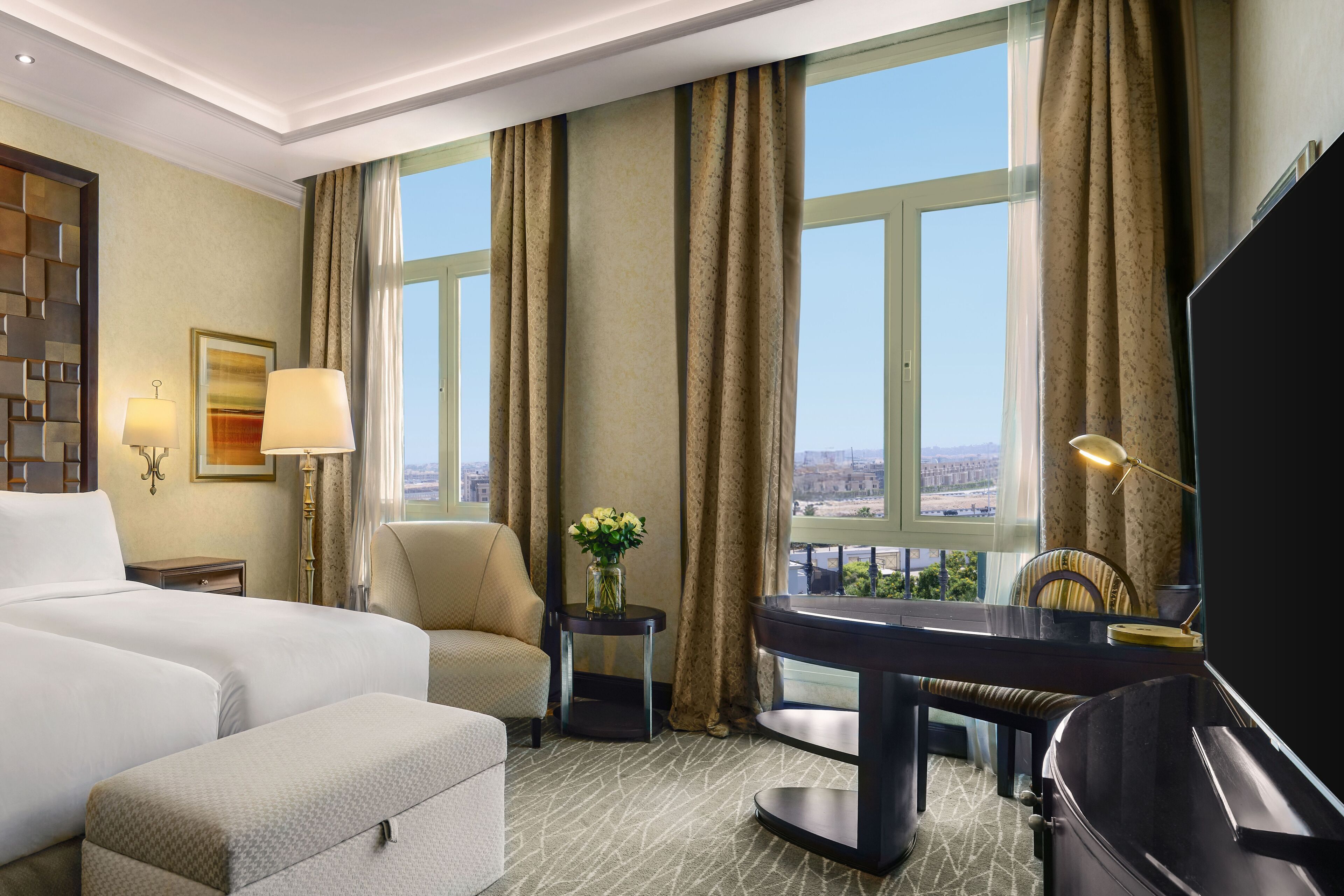 A hotel room with a bed, a desk, a chair, a TV, and a view of the city.