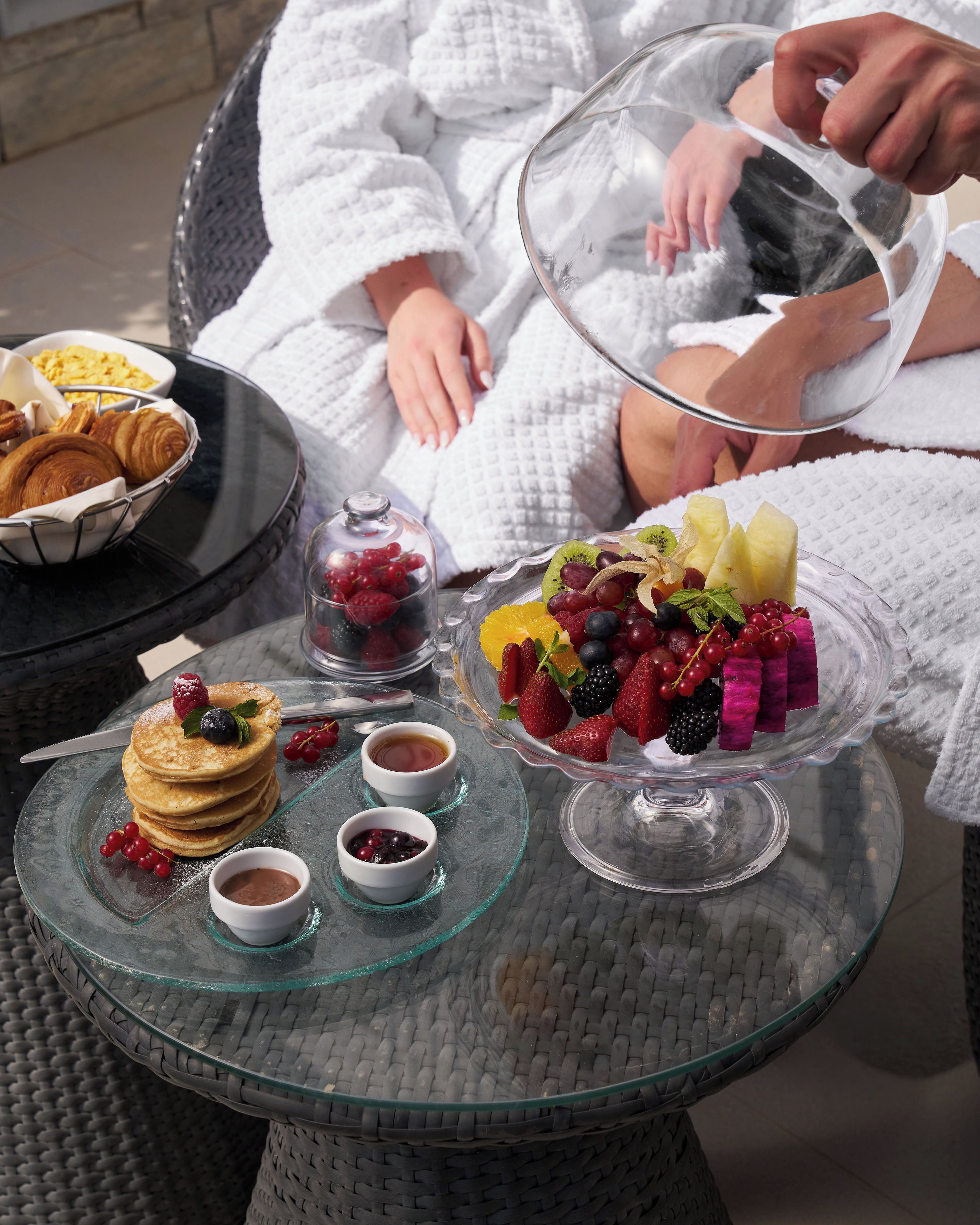 A breakfast setting with pancakes, berries, and fruit on a glass table.