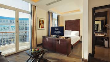 Een hotelkamer met een groot bed, een televisie, een bureau met een laptop en uitzicht op de stad door grote ramen.