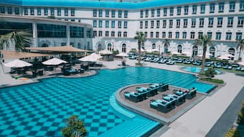 Een groot hotel met een centraal gelegen zwembad, terras en palmbomen.