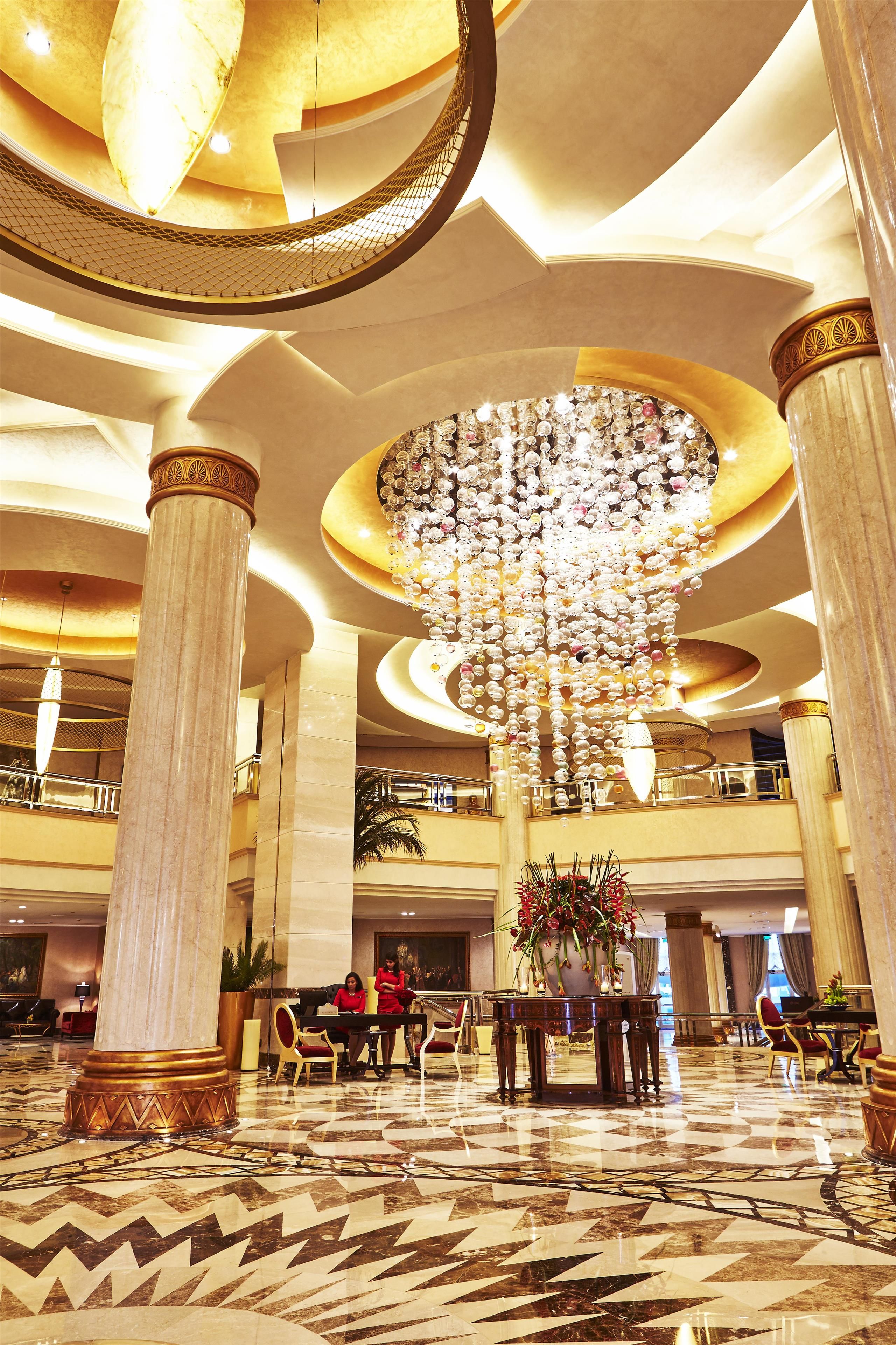 A spacious lobby with high ceilings, large columns, and a grand chandelier.