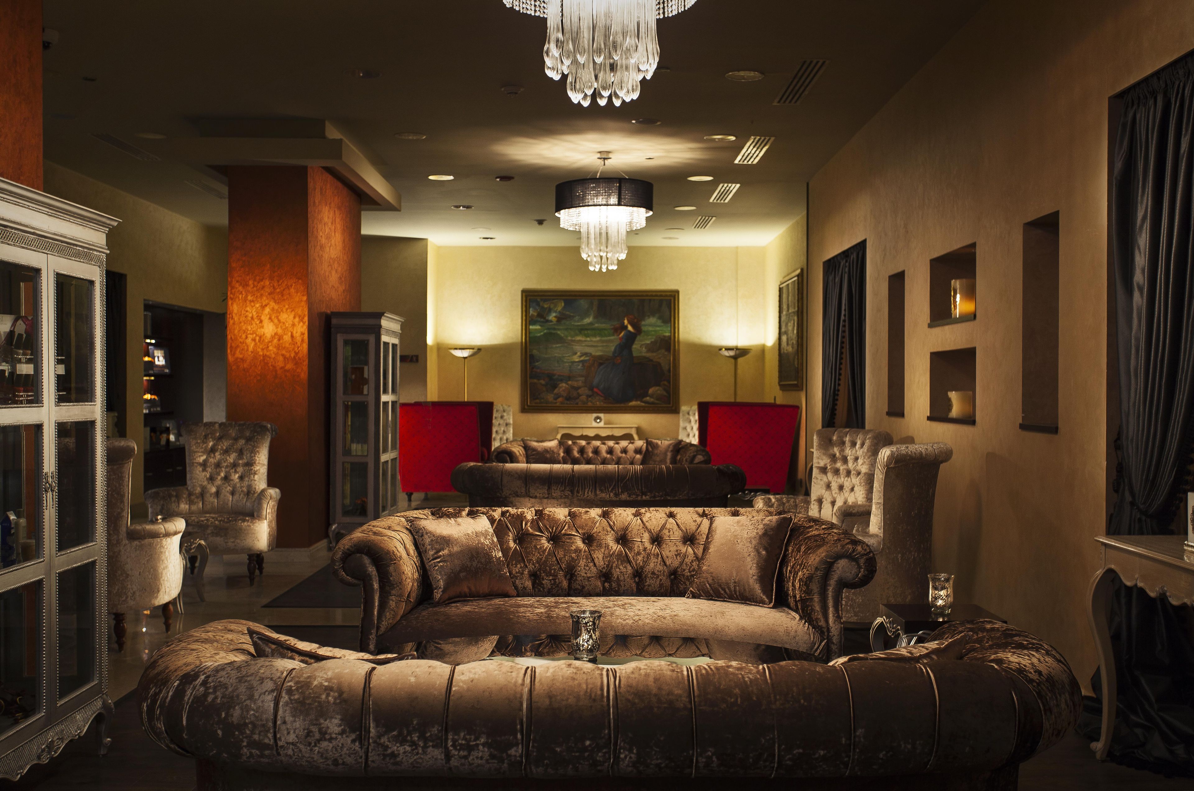A luxurious living room with a large, ornate sofa, a chandelier, and a painting on the wall.