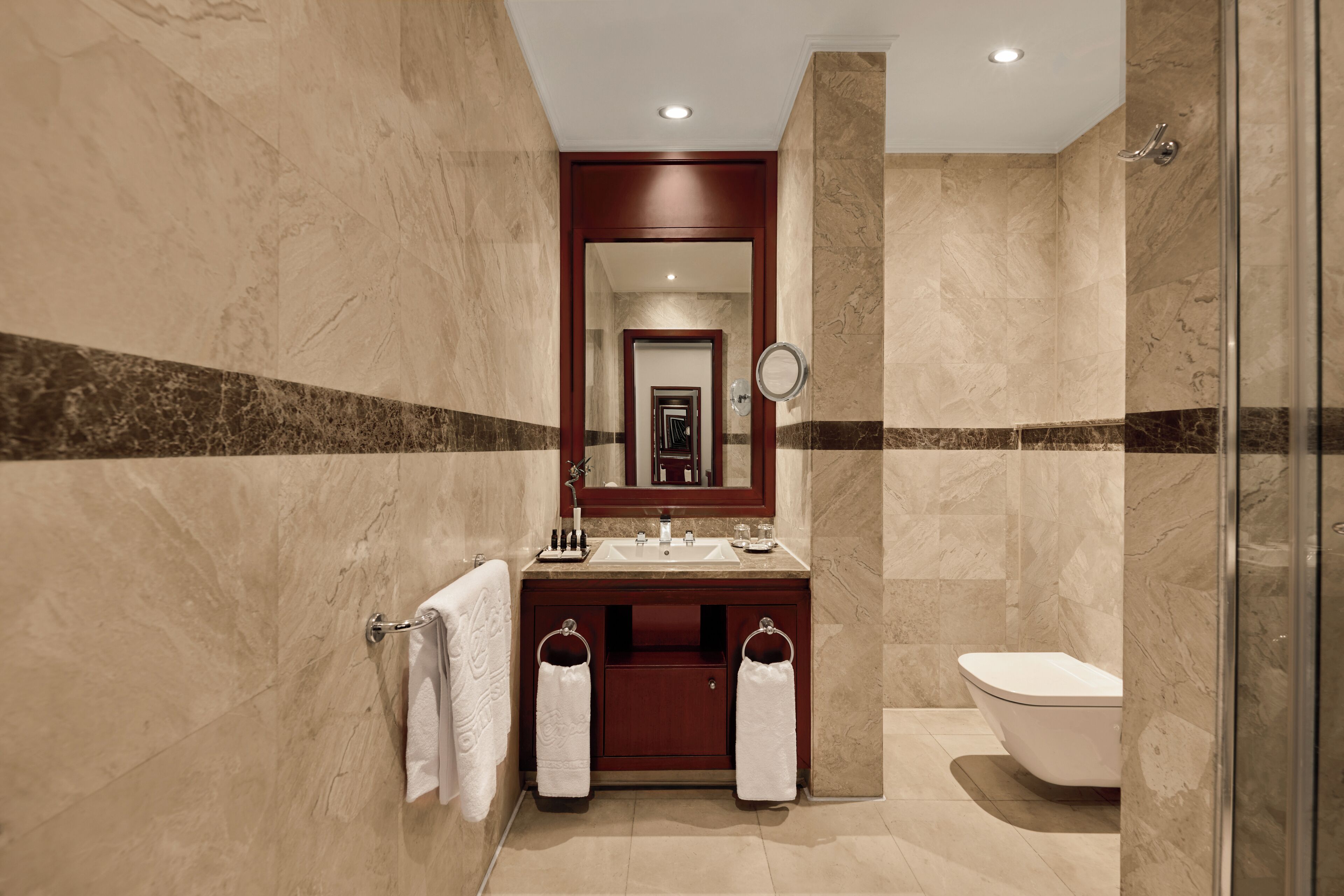 Un baño moderno con piso de mármol, tocador de madera, cerramiento de ducha de vidrio y un espejo grande.